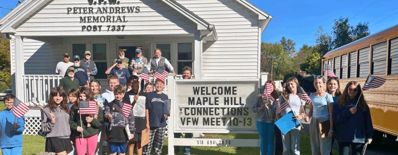 A large group of Maple Hill students holding American flags and posing with a group of veterans on the porch of the V.F.W. Peter Andrews Memorial Post 7337.