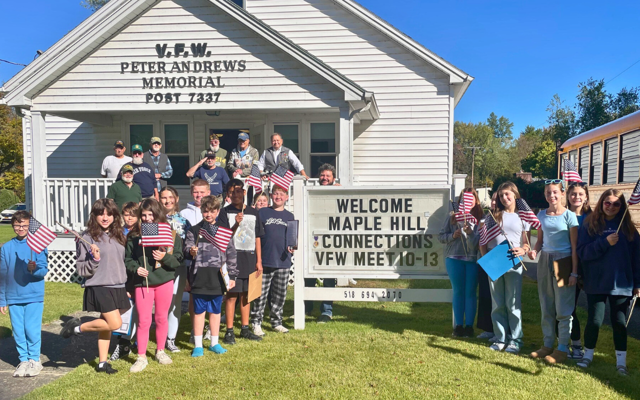 A large group of Maple Hill students holding American flags and posing with a group of veterans on the porch of the V.F.W. Peter Andrews Memorial Post 7337.