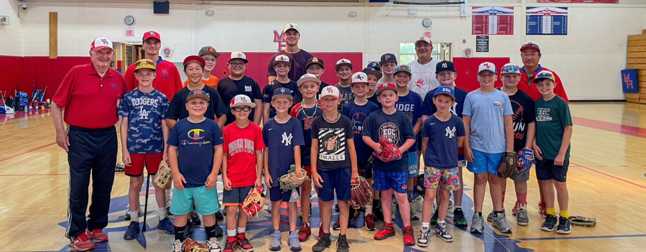 Group photo of Schodack students and coaches in baseball hats and uniforms posed together in the school gymnasium.
